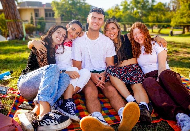 a group of 5 students sit on a blanket on the mounds in a group hug